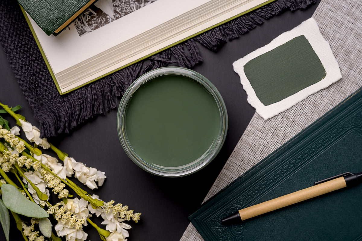 Green cup of paint, notebook, pen, and flowers on a dark surface