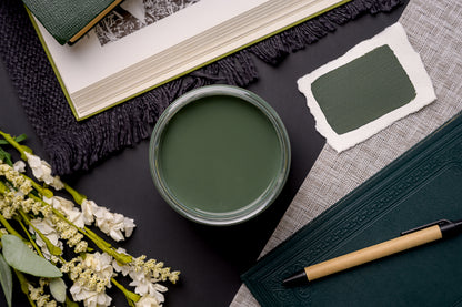 Green cup of paint, notebook, pen, and flowers on a dark surface