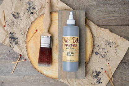 Up In Smoke VooDoo Gel Stain bottle with a brush on a wooden surface