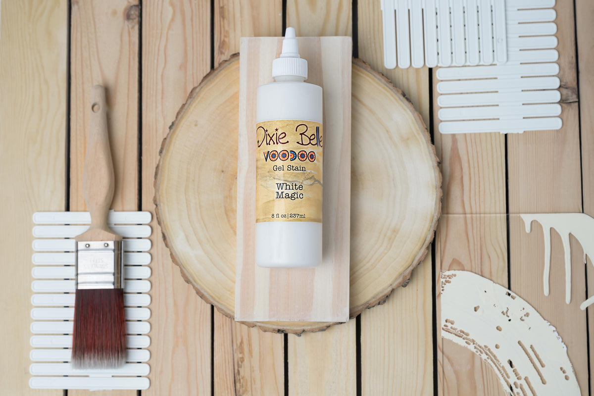 A bottle of White Magic VooDoo Gel Stain on a wooden surface with a brush and paint samples.
