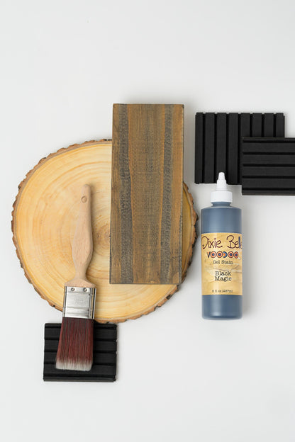Wooden surface with a brush, sandpaper, and bottle of wood finish on a white background with Black Magic Voodoo Gel Stain