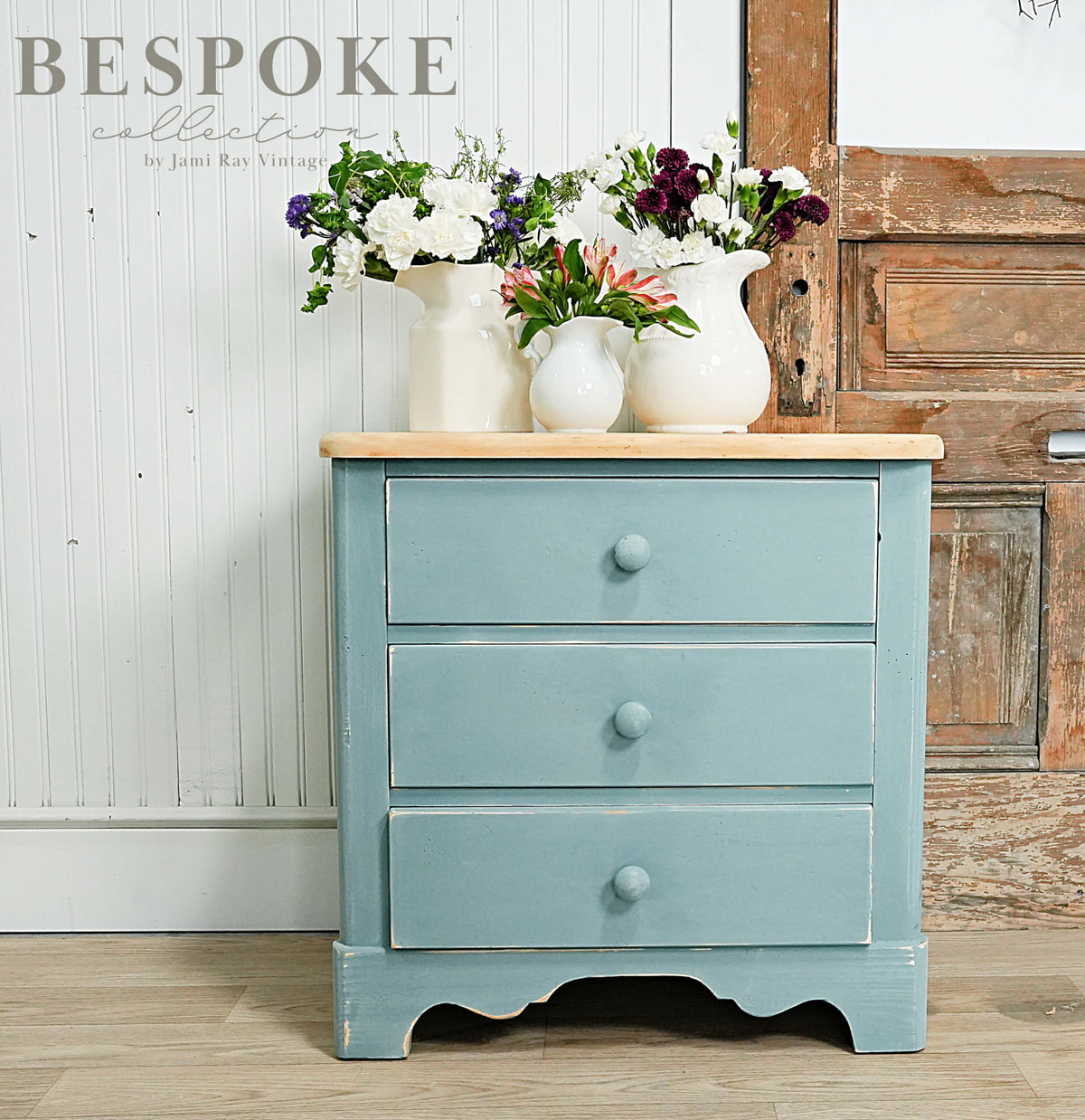 Vintage-style blue dresser with wooden top against a rustic wooden wall.