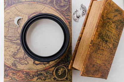 Moon Beam Terra Clay Paint on top of an antique-style illustrated book, with a matching brown textured box beside it and small silver celestial charms on a light surface.