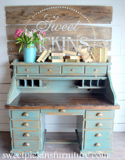Vintage-style desk with wooden top and blue-painted drawers, decorated with flowers and books.
