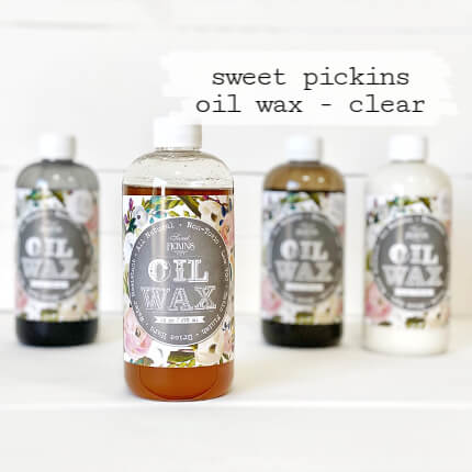 Four bottles of Sweet Pickins Oil Wax arranged on a white surface against a white background, with the center bottle labeled 'clear' and the text 'sweet pickins oil wax - clear' above it.