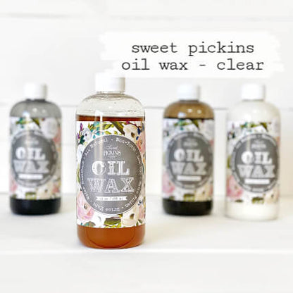Four bottles of Sweet Pickins Oil Wax arranged on a white surface against a white background, with the center bottle labeled 'clear' and the text 'sweet pickins oil wax - clear' above it.