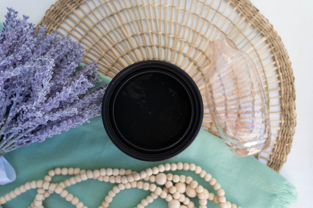 Onyx Terra Clay Paint, placed on a mint green cloth with wooden beads, dried lavender, a woven placemat, and a clear glass shell around it.