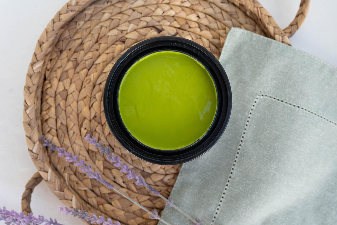 Pistachio Terra Clay Paint, placed on a woven straw mat next to a light gray cloth and lavender sprigs.