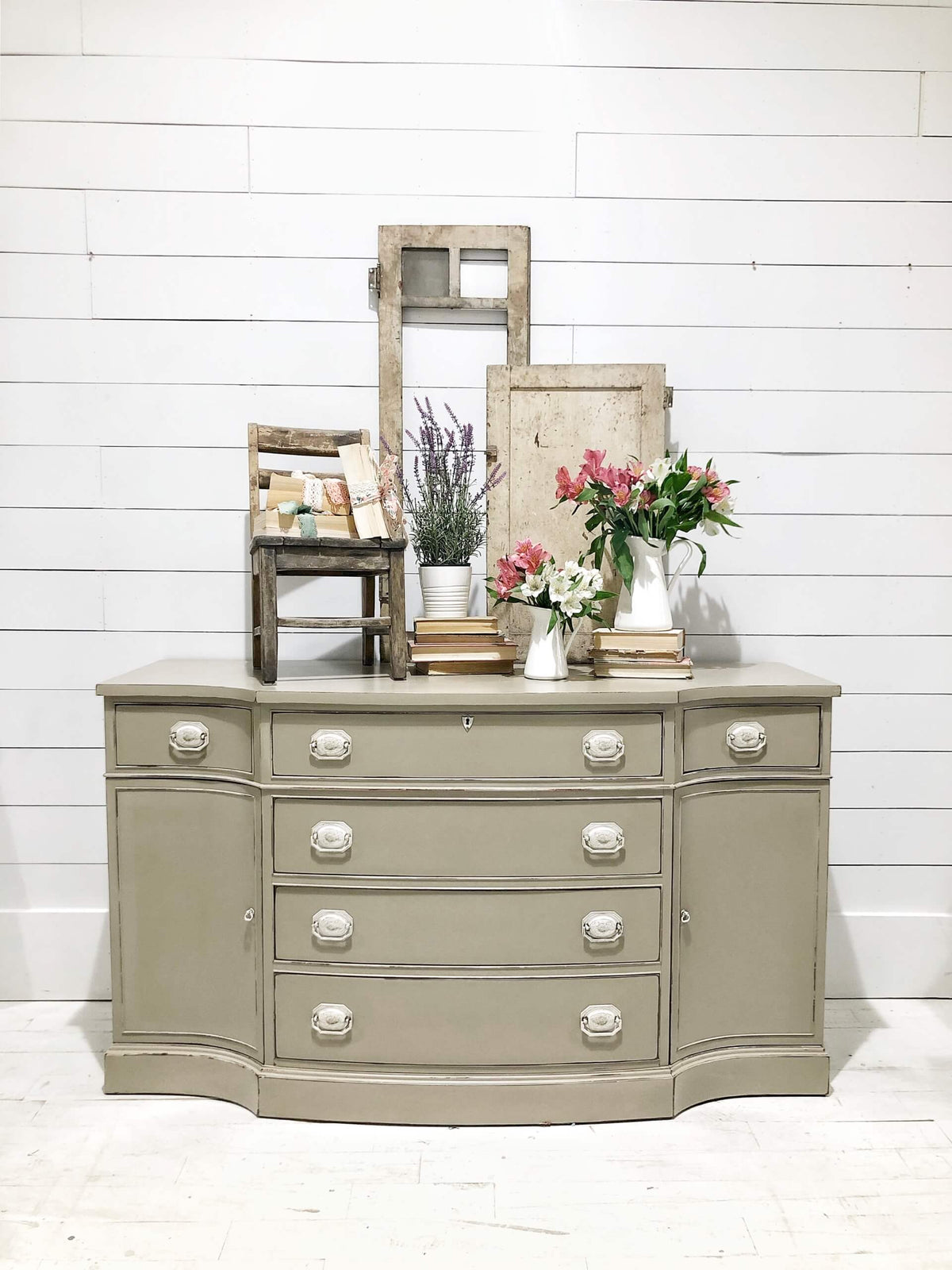 Taupe dresser with decorative items against a white wooden wall