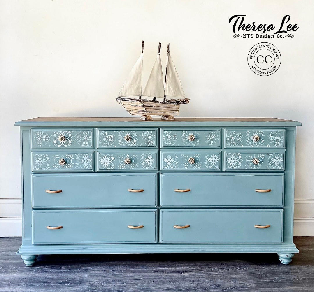 Blue dresser with decorative elements and a ship model on top, featuring the Theresa Lee NTS Design Co. logo.