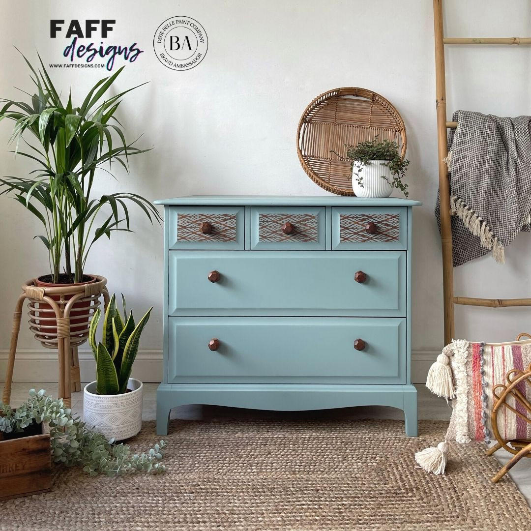 A light blue painted wooden chest of drawers with three upper drawers and two larger lower drawers, styled in a boho room setting with potted plants, a woven basket, and a ladder chair.