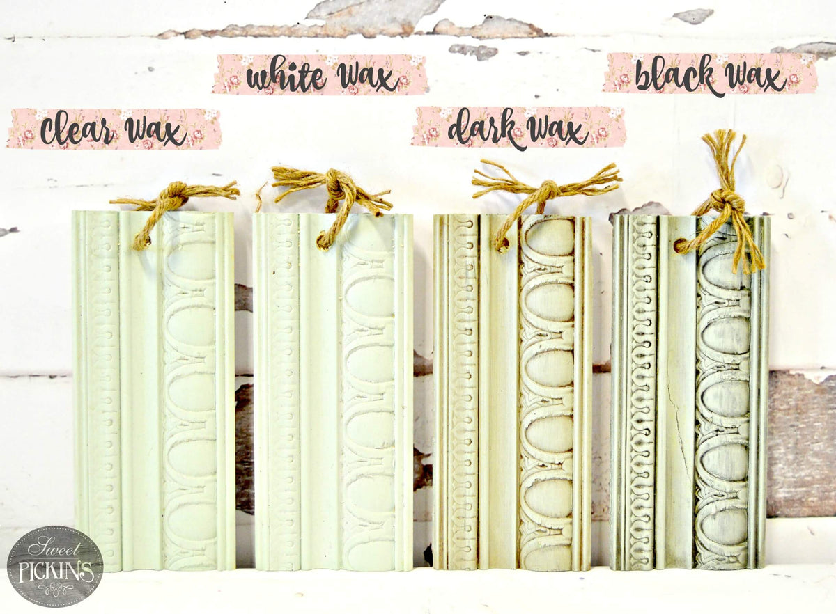 Six decorative carved wood molding pieces in pale green, cream, and dark green shades, each tied with twine and labeled above as clear wax, white wax, black wax, clear wax, dark wax, and white wax. The pieces are arranged on a distressed white wood background with a Sweet Pickings logo in the lower left corner.